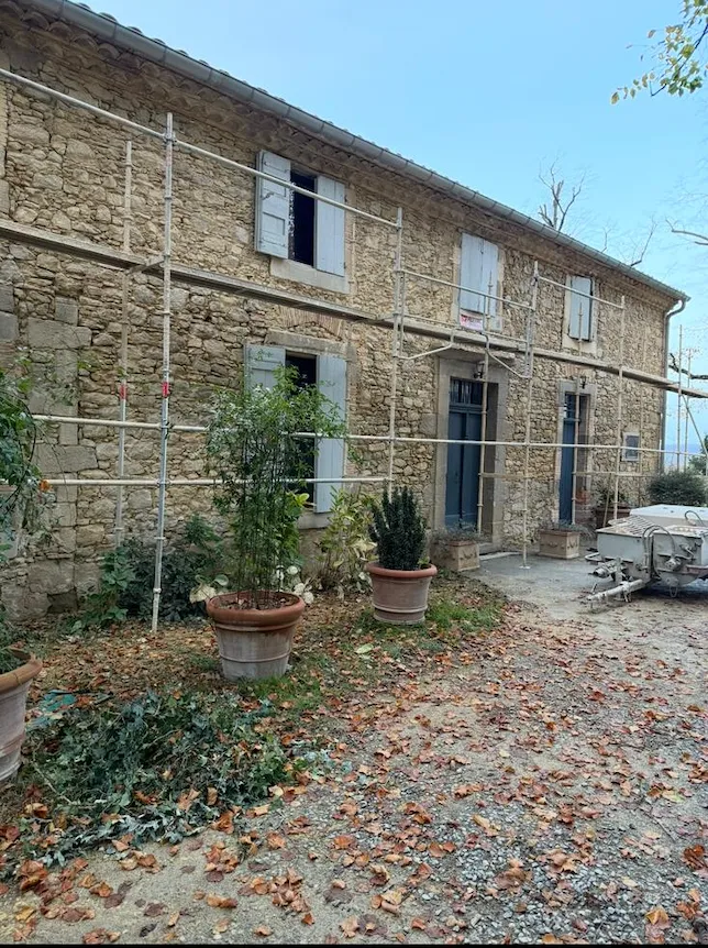 Rénovation d’une maison en pierre avec échafaudage par Milo facade en Haute-Garonne, volets bleus et pots de plantes