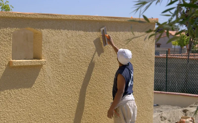 Ouvrier appliquant un enduit sur façade jaune Milo facade en Haute-Garonne sous un ciel bleu