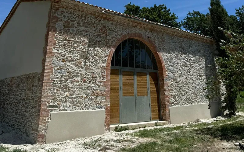 Façade en pierre rénovée par Milo facade en Haute-Garonne, grange rustique avec porte bois métal et toit tuiles rouges