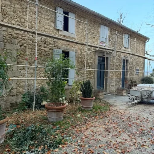 Rénovation d’une maison en pierre avec échafaudage par Milo facade en Haute-Garonne, volets bleus et pots de plantes