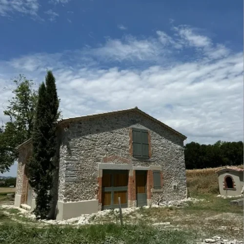 Maison rurale en pierre rénovée par Milo facade dans la campagne de Haute-Garonne sous ciel bleu et champs verdoyants