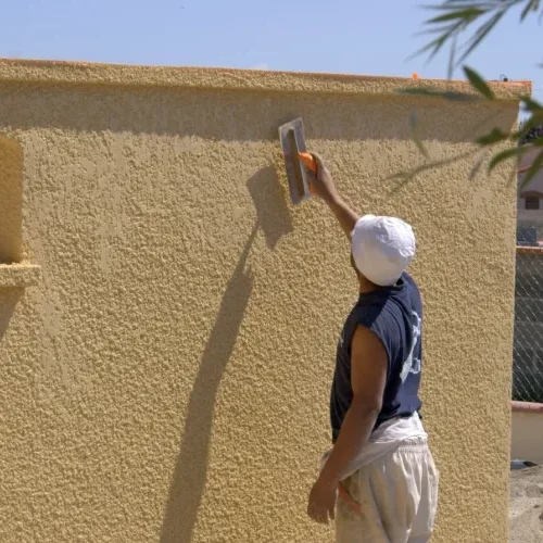 Ouvrier appliquant un enduit sur façade jaune Milo facade en Haute-Garonne sous un ciel bleu