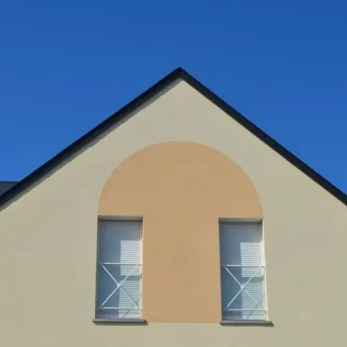 Façade moderne beige rénovée par Milo facade en Haute-Garonne, pignon gris et fenêtres aux volets blancs