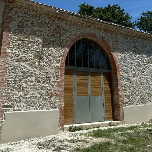 Façade en pierre rénovée par Milo facade en Haute-Garonne, grange rustique avec porte bois métal et toit tuiles rouges